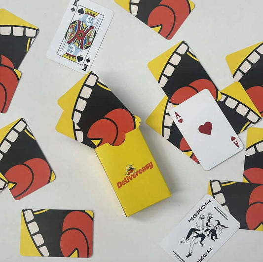 Custom poker-sized playing cards with vibrant designs and a branded yellow box, featuring jokers, aces, and king on display.