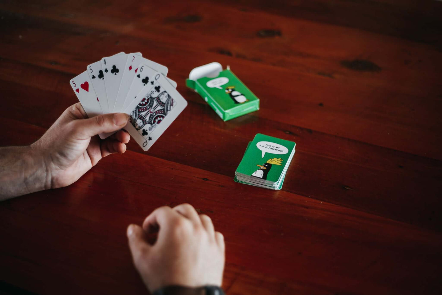 Person holding a fan of custom printed playing cards with a green deck on a wooden table.