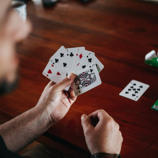 Person holding a hand of custom poker-sized playing cards at a wooden table.