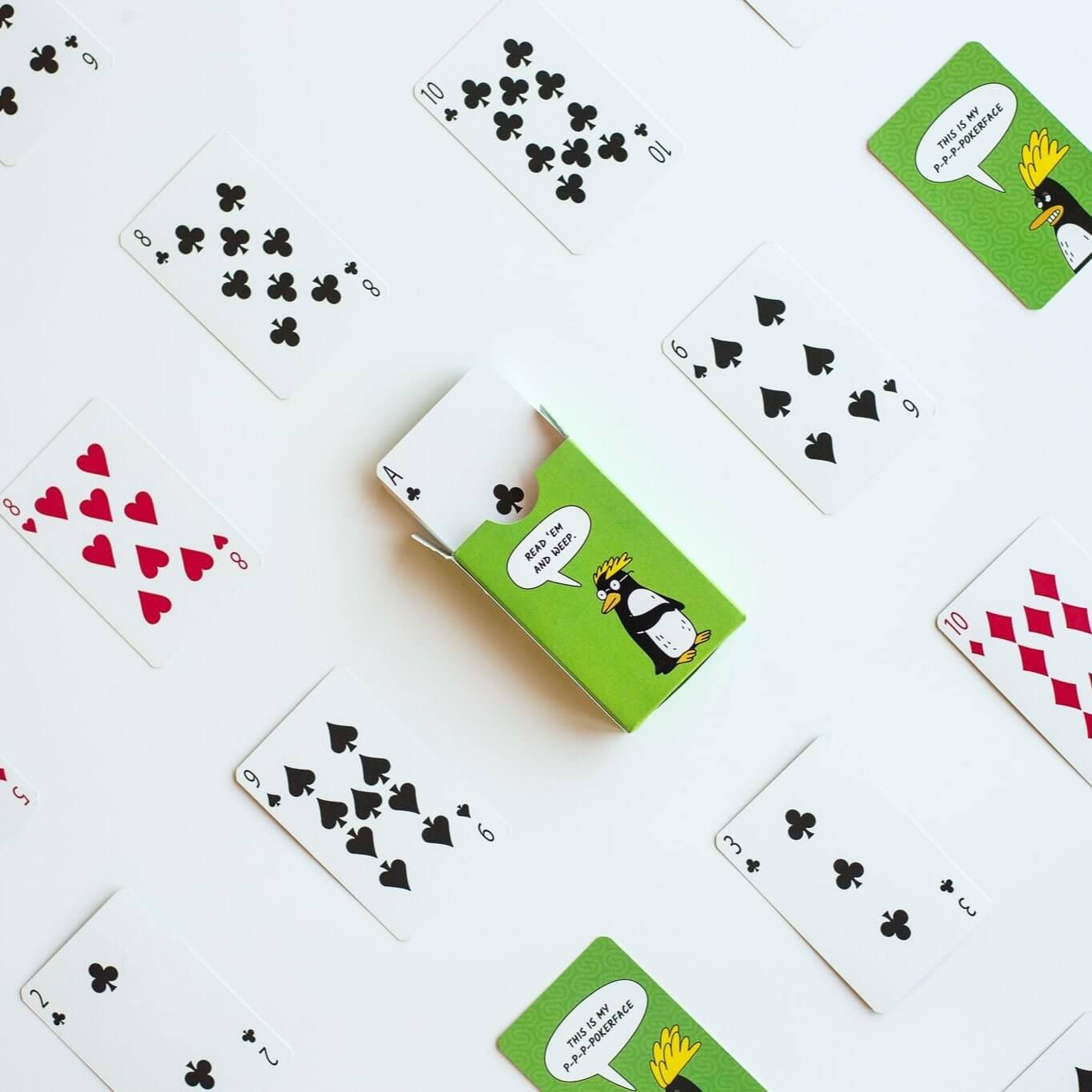 Custom poker-sized playing cards with penguin design, scattered on a white surface, showcasing card variety and playful art.
